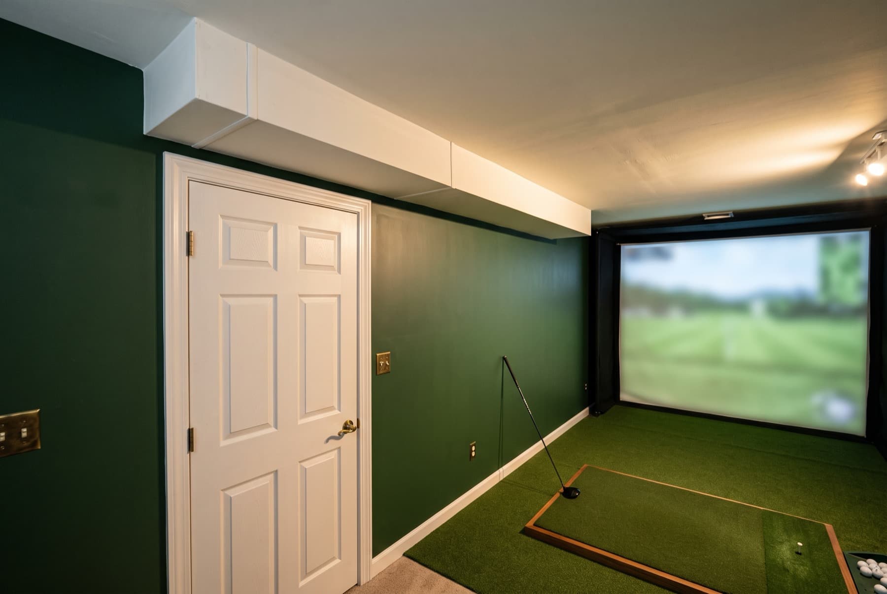 A green golf room with a boxed duct running across a low ceiling, level with the head of the door beside it.
