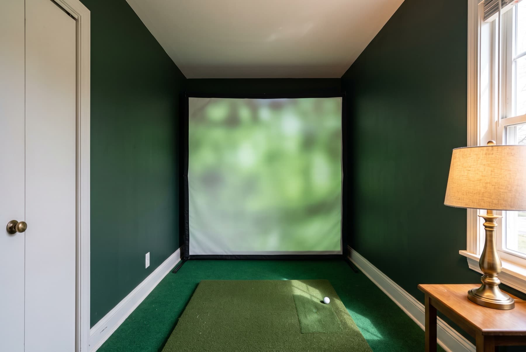 A spare bedroom converted for golf, with the screen close enough to the mat that the room clearly has no depth left.
